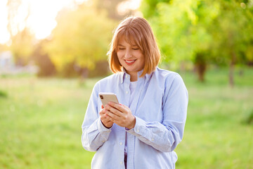 Photo portrait female student in blue shirt keeping cellphone browsing internet walking along summer park
