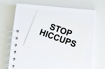 STOP HICCUPS inscription on a white card that lies on a notebook, medical concept