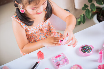 Asian adorable funny little girl making makeup dips brush into bottle to paints nails polish red...