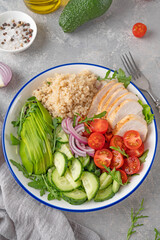 Healthy bowl lunch with grilled chicken, quinoa, avocado, tomatoes, cucumbers and fresh arugula on gray background. Top view. Selective focus.