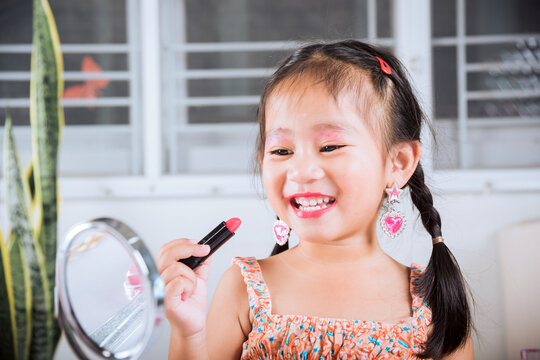 Happy kid is beautiful make up with cosmetics toy, Asian adorable funny little girl making makeup her face she looking in the mirror and applying red lipstick to mouth, Learning activity to be woman