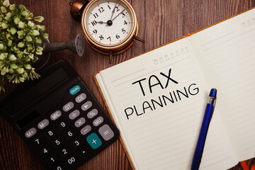 Tax Planning typography text on paper card with alarm clock and calculator on wooden background