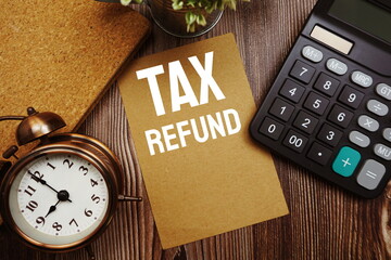 Tax Refund typography text on paper card with alarm clock and calculator on wooden background - obrazy, fototapety, plakaty