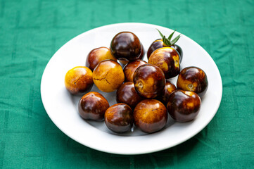 fresh cherry tomatoes of different varieties on a plate on the blurred background, closeup