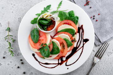 Caprese salad with tomatoes, mozzarella cheese, basil and balsamic sauce on a white plate on the kitchen table. top view