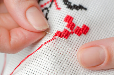 A woman embroiders the national symbols of Ukraine with a cross. Close-up of female hands cross-stitching on white canvas.
