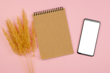 Smartphone with blank white display and notepad with craft paper on pink background