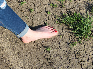 Woman's foot in jeans on background of cracked ground and grass