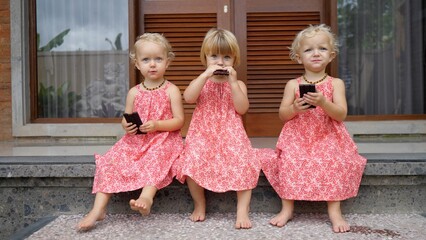 Three cute toddler girls sitting on the terrace and eating organic chocolate bars, enjoying their freedom, carefree and innocent friendship