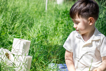 cute little boy with stack of toilet wc paper in tall green grass.kid is smiling or holding toilet...