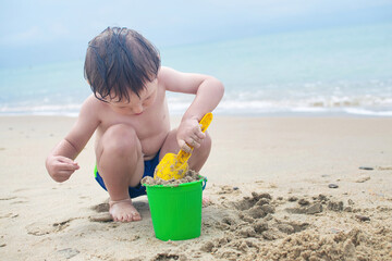 Wonderful boy plays with a bucket and a shovel in the sand on the seashore.