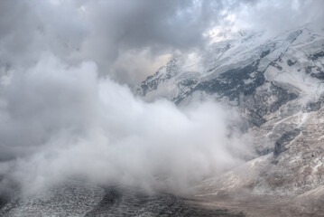 Obraz premium A large cloud hangs over the glacier. In the background is a high mountain with snow-capped peaks. A large area of â€‹â€‹the frame is occupied by a hazy image of a cloud. soft focus.