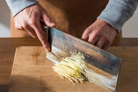 Chef take a kitchen knife cut ginger silk on the cutting board only hands no face