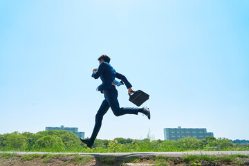 青空の下を走るビジネスマンの後ろ姿