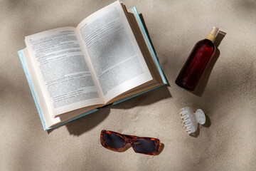 leisure and summer holidays concept - open book, sunscreen, hair clip and sunglasses on beach sand - obrazy, fototapety, plakaty