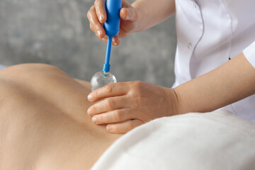Masseur in cabinet massaging back muscles of woman lying down on couch with medical vacuum cups closeup. Specialist reception, professional massage and relaxation in clinic. Cupping and treatment