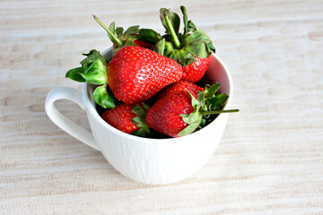 organic strawberries in white cup on beige background, close-up