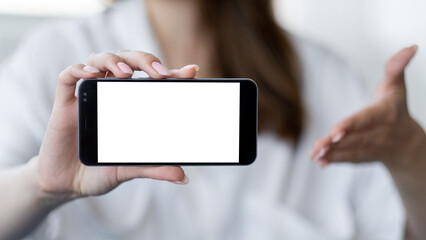 Mobile connection. Advertising mockup. Digital life. Unrecognizable defocused man holding and pointing to smartphone with blank screen in light room interior.