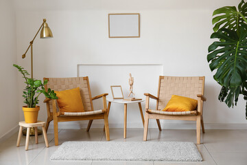Comfortable armchairs, table and houseplant near light wall