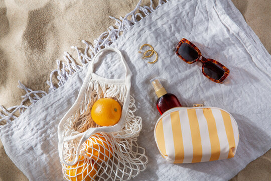 leisure and summer holidays concept - bag of oranges and sunscreen oil on beach blanket
