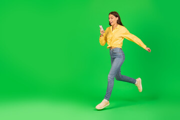 Excited Woman Using Smartphone Running And Communicating Over Green Background