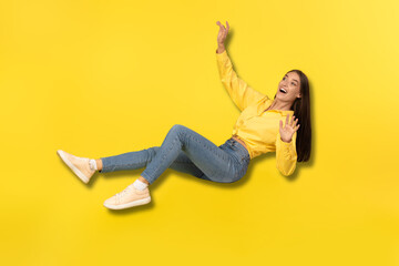 Excited Young Woman Falling In Mid Air Over Yellow Background