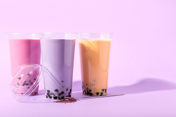 Plastic cups of different tasty bubble tea on purple background