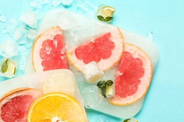 Fresh slices of citrus fruits frozen in ice on turquoise background