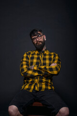 Fototapeta na wymiar Tattooed man with a beard wearing checkered shirt is posing seated on a chair in a studio
