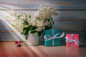 Still Life with Gift boxes and Bouquet of Flowering Lilacs in sun rays over wooden background