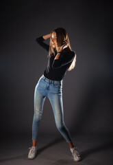 Attractive female model in denim jeans posing isolated on grey background.
