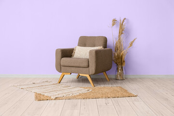 Comfortable armchair and vase with reed flowers near violet wall in room interior
