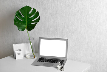 Workplace with laptop, palm leaf in vase and calendar near light wall
