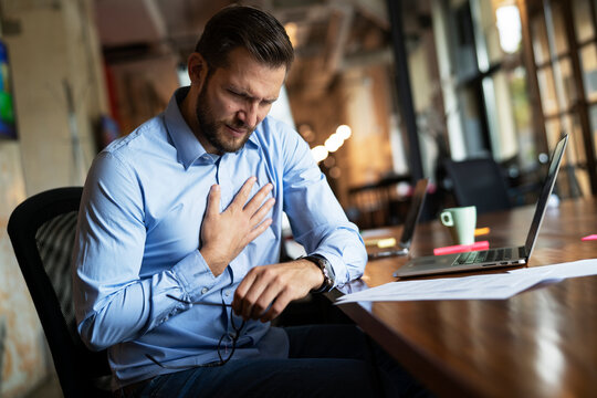 oung businessman having chest pain. Man sitting in the office working on laptop.
