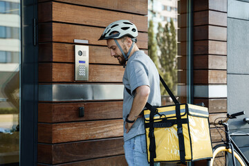 Express food delivery courier with insulated bag using intercom. - obrazy, fototapety, plakaty