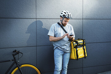 Express food delivery courier with insulated bag looking at phone. - obrazy, fototapety, plakaty