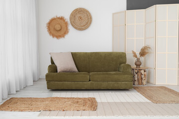 Interior of light living room with green sofa, folding screen and decor