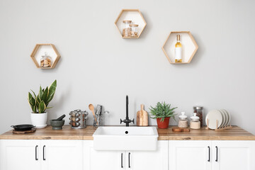 Fototapeta na wymiar Counters with sink, kitchen utensils and houseplants near light wall