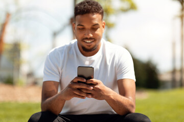 Happy black man texting message, checking app and social media on cellphone in city park outdoors,...