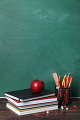 School stationery with books and apple on table near green chalkboard © Pixel-Shot