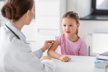 Fototapeta premium medicine, healthcare and vaccination concept - female doctor or pediatrician disinfecting arm skin of little girl patient at clinic