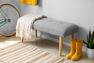 Soft bench with plaid, gumboots and houseplant near light wall