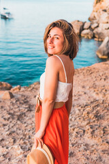 Smiling young woman on holiday, hat in hand in the cove of Portal Vells, island of Palma de Mallorca, Spain.