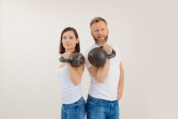 Young athletic woman and man lifting up and holding kettlebells, white background. Keeping fit by...