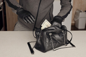 Robber in black outfit and gloves see in opened stolen women bag. The thief takes out US dollar...