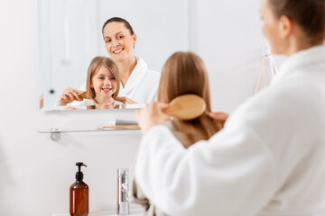 beauty, hygiene, morning and people concept - happy smiling mother and little daughter with hairbrush brushing hair at bathroom