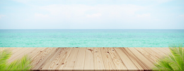 Fototapeta premium Palm leaves with wooden on sea.blank table on blue water shore and blue sky at coast. sunlight blur bokeh on ocean. mockup tropical seaside. Tourism relax vacation travel summer holidays.
