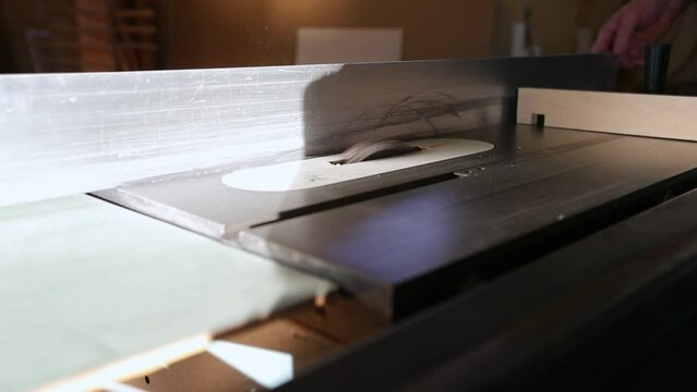 A craftsman starts up a table saw and cuts a groove in piece of wood using a dado set in slow motion.