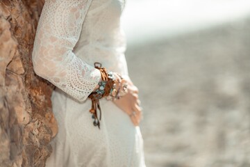 Middle aged woman looks good with blond hair, boho style in white long dress on the beach decorations on her neck and arms.