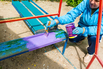 A woman paints a bench on the playground in kindergarten